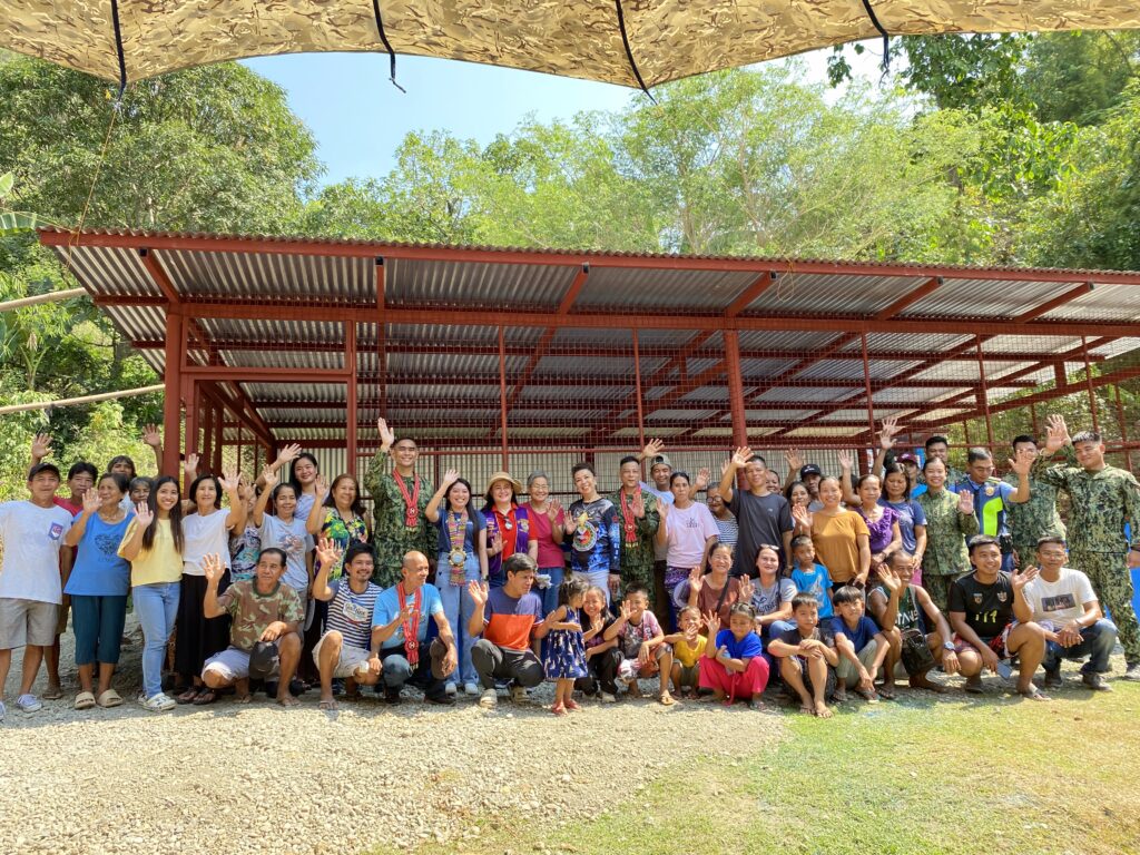 A group image where people smile and some wave their hands in front of a newly-built warehouse